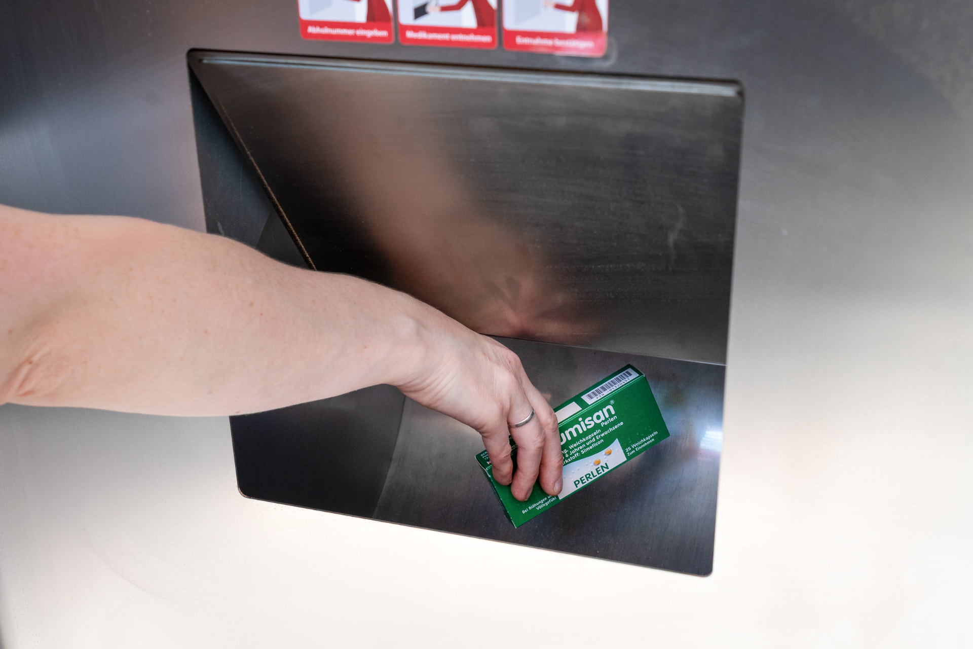Hand entnimmt eine Medikamentenpackung aus der Klappe des Abholautomaten