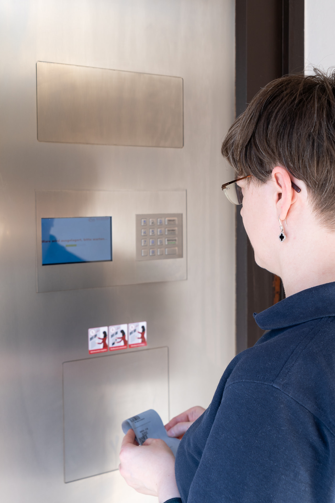 Kundin wartet vor dem Abholautomaten, während die Ware ausgelagert wird