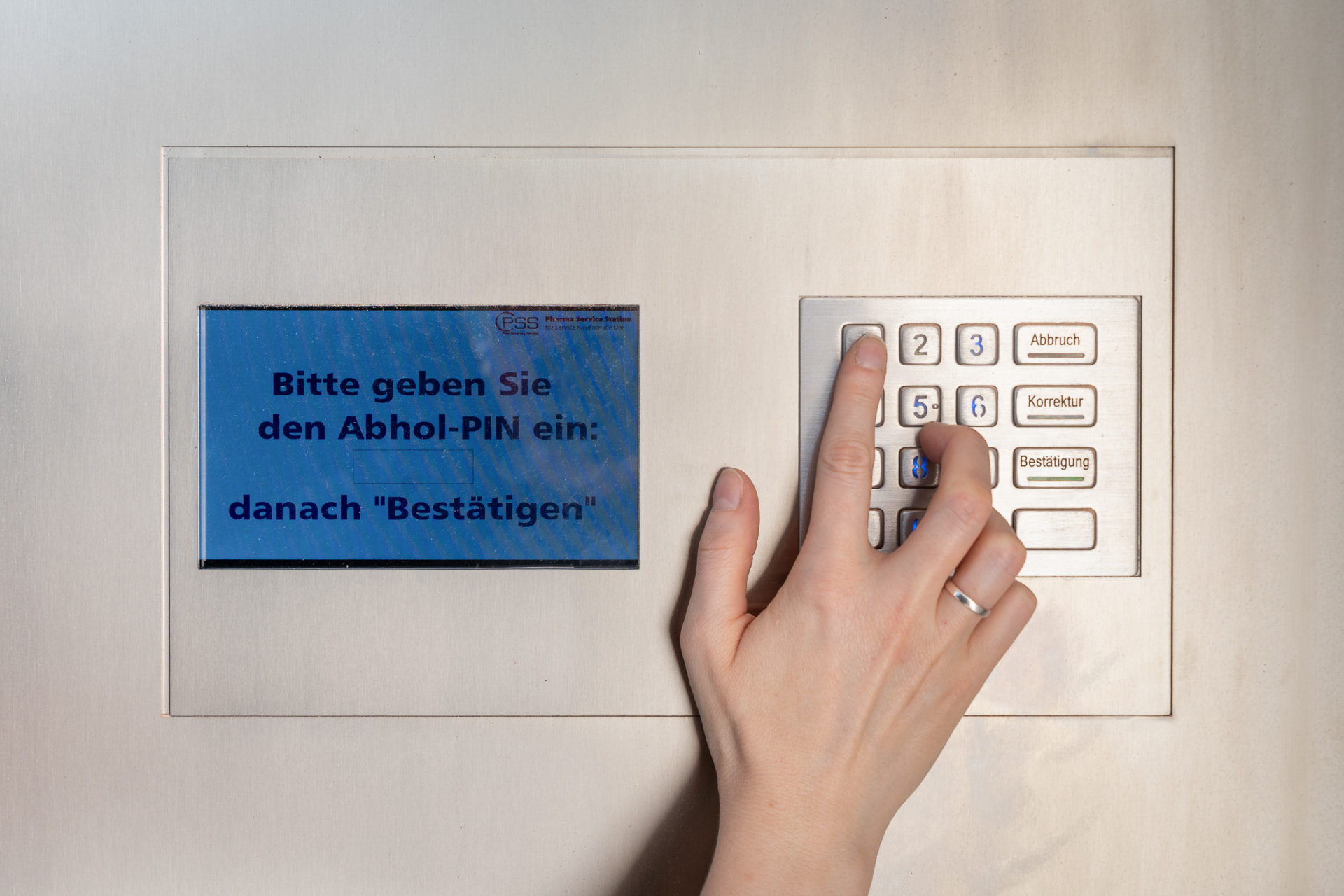 Hand gibt den Abhol-PIN am Tastenfeld des Abholautomaten ein
